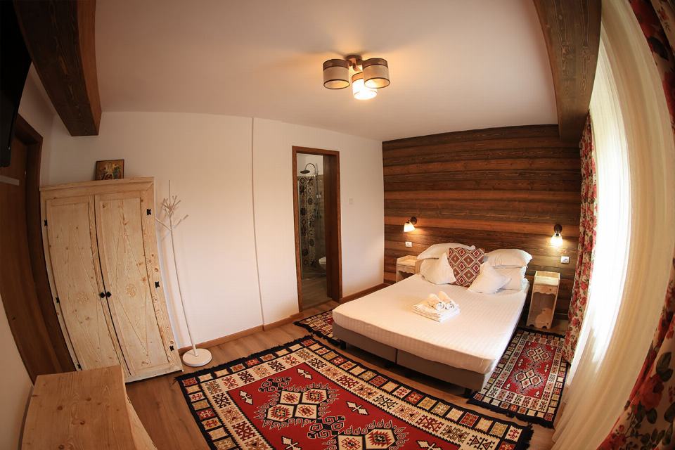 Apartamentul 1 din Vila Rebeca, cu pat matrimonial și canapea extensibilă, lambriu de lemn și covor tradițional bucovinean