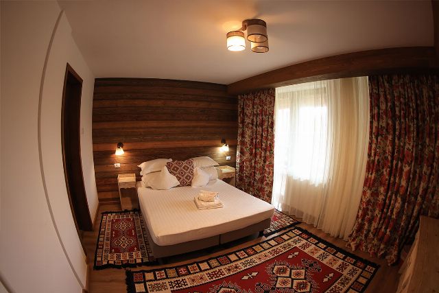 Apartamentul 1 din Vila Rebeca, văzută dinspre ușă, cu pat matrimonial și canapea extensibilă și noptiere de lemn masiv