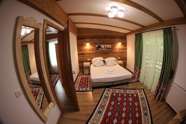 Apartamentul 2 din Vila Rebeca, cu pat matrimonial și canapea extensibilă, lambriu de lemn și covor tradițional bucovinean
