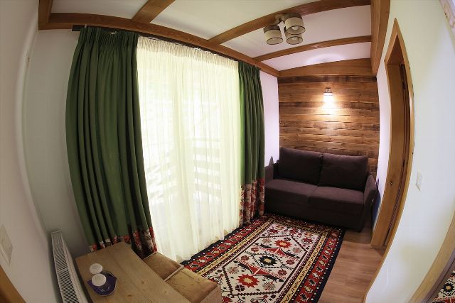 Spațiul de zi al apartamentului 3 din Vila Rebeca, cu canapea, televizor și fereastră mare