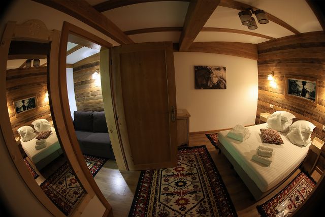 Apartamentul 3 din Vila Rebeca, cu pat matrimonial și canapea extensibilă, lambriu de lemn și covor tradițional bucovinean