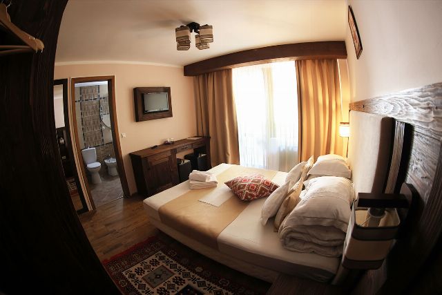 Camera 1 din Vila Rebeca, văzută dinspre ușă, cu pat matrimonial și noptiere de lemn masiv