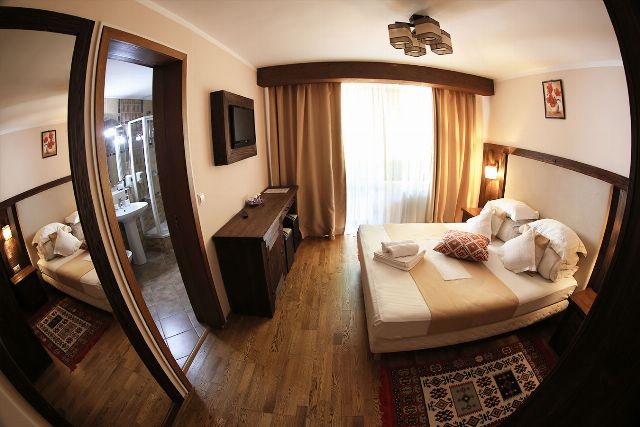 Camera 1 din Vila Rebeca, cu pat matrimonial, veioze de perete și fereastră cu perdele deschise