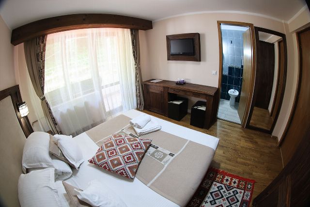 Camera 2 din Vila Rebeca, văzută dinspre ușă, cu pat matrimonial și noptiere de lemn masiv