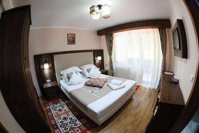 Camera 2 din Vila Rebeca, cu pat matrimonial, veioze de perete și fereastră cu perdele deschise