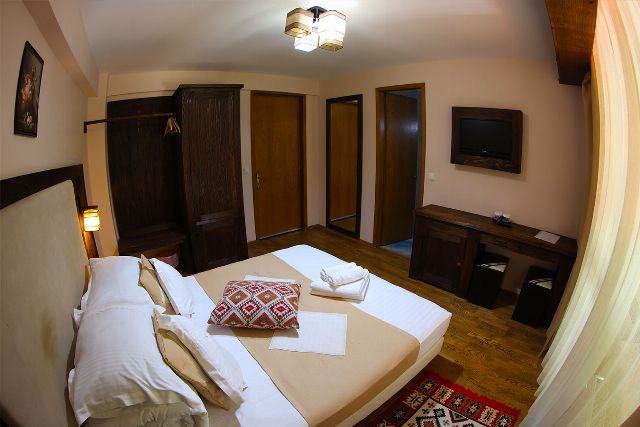 Camera 4 din Vila Rebeca, cu pat matrimonial, lambriu de lemn și covor tradițional bucovinean