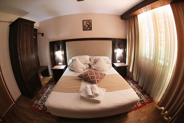 Camera 5 din Vila Rebeca, cu pat matrimonial, lambriu de lemn și covor tradițional bucovinean