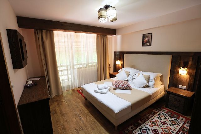 Camera 5 din Vila Rebeca, cu pat matrimonial, veioze de perete și fereastră cu perdele deschise